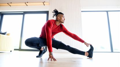 A portrait of fit mixed race man with dreadlocks doing exercise at home, stretching