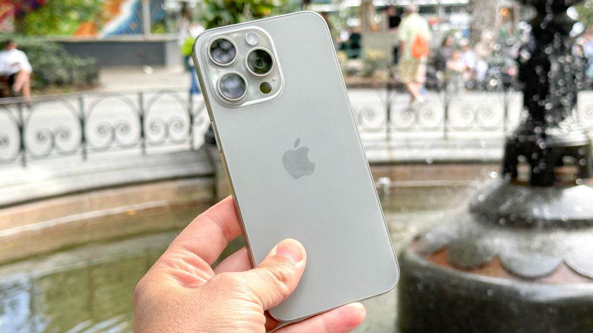 iPhone 15 Pro Max in hand in front of a fountain