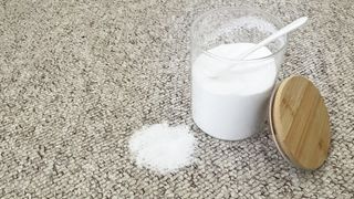 Glass container of baking soda on carpet to test cleaning with baking soda