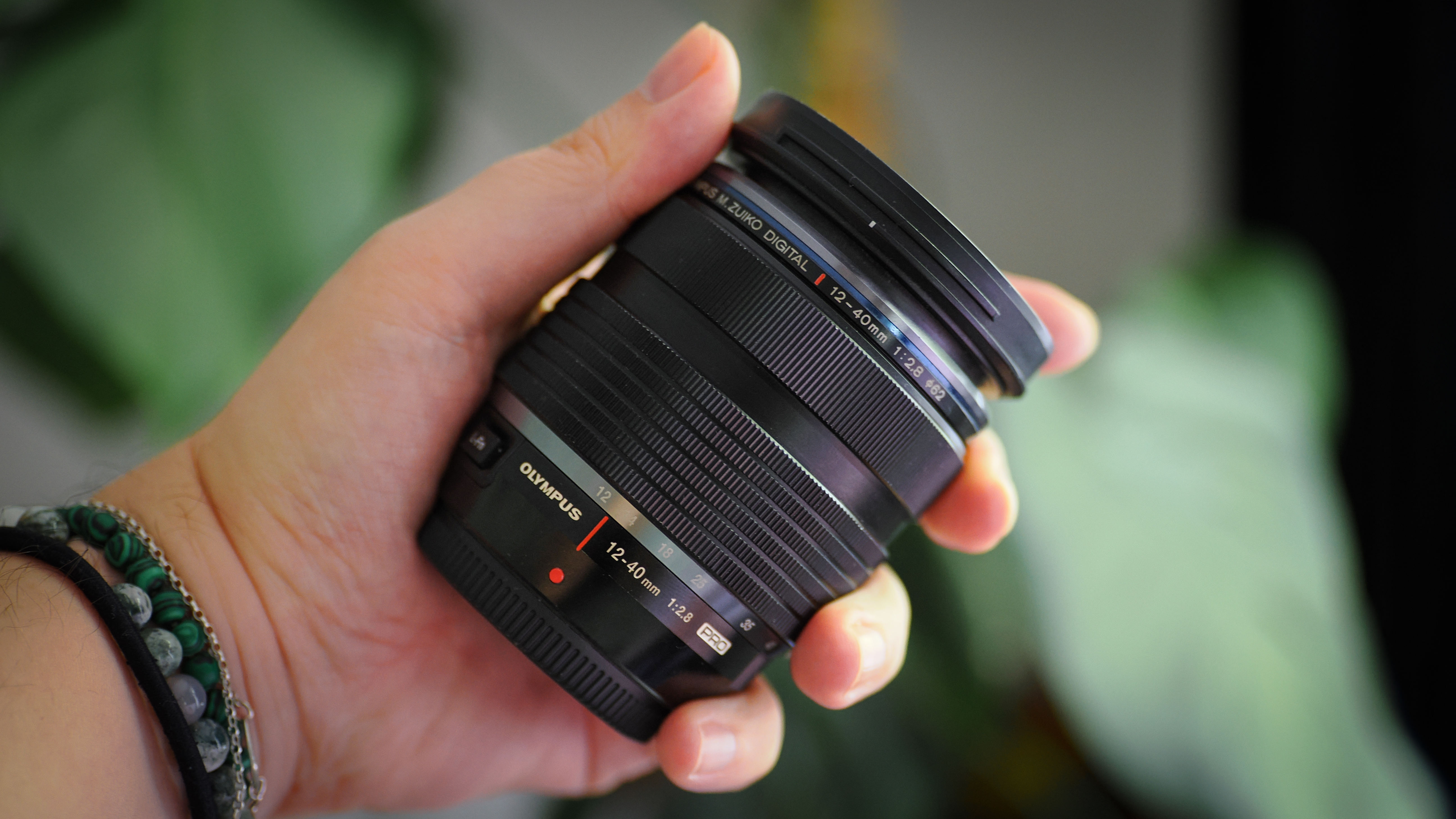 Olympus M.Zuiko 12-40mm f/2.8 Pro lens being held in hand, in front of foliage
