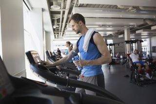 Person adjusting the settings on a treadmill in a gym