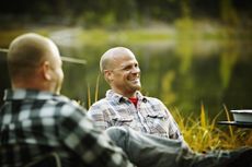 Man sitting in discussion with friends by lake smiling and laughing.
