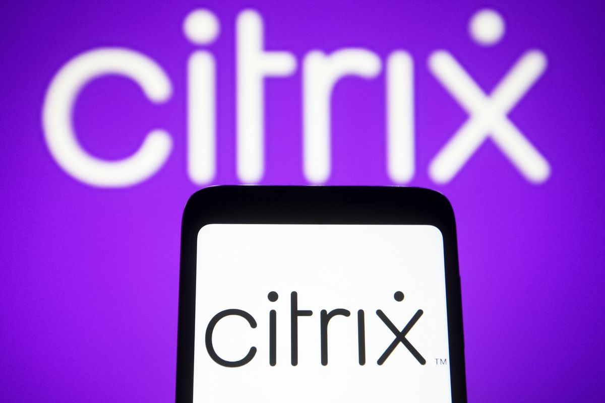 The Citrix logo (the word &quot;Citrix&quot;) on a phone against a white background, while in the background the logo is lit up in white text on a purple background.