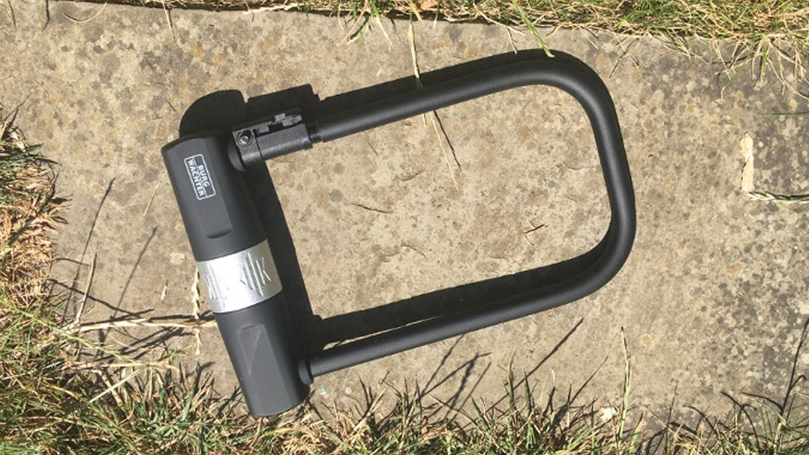 A black Burg Wachter 1580 HB D-lock with silver keyhole cover pictured on stone paving slab