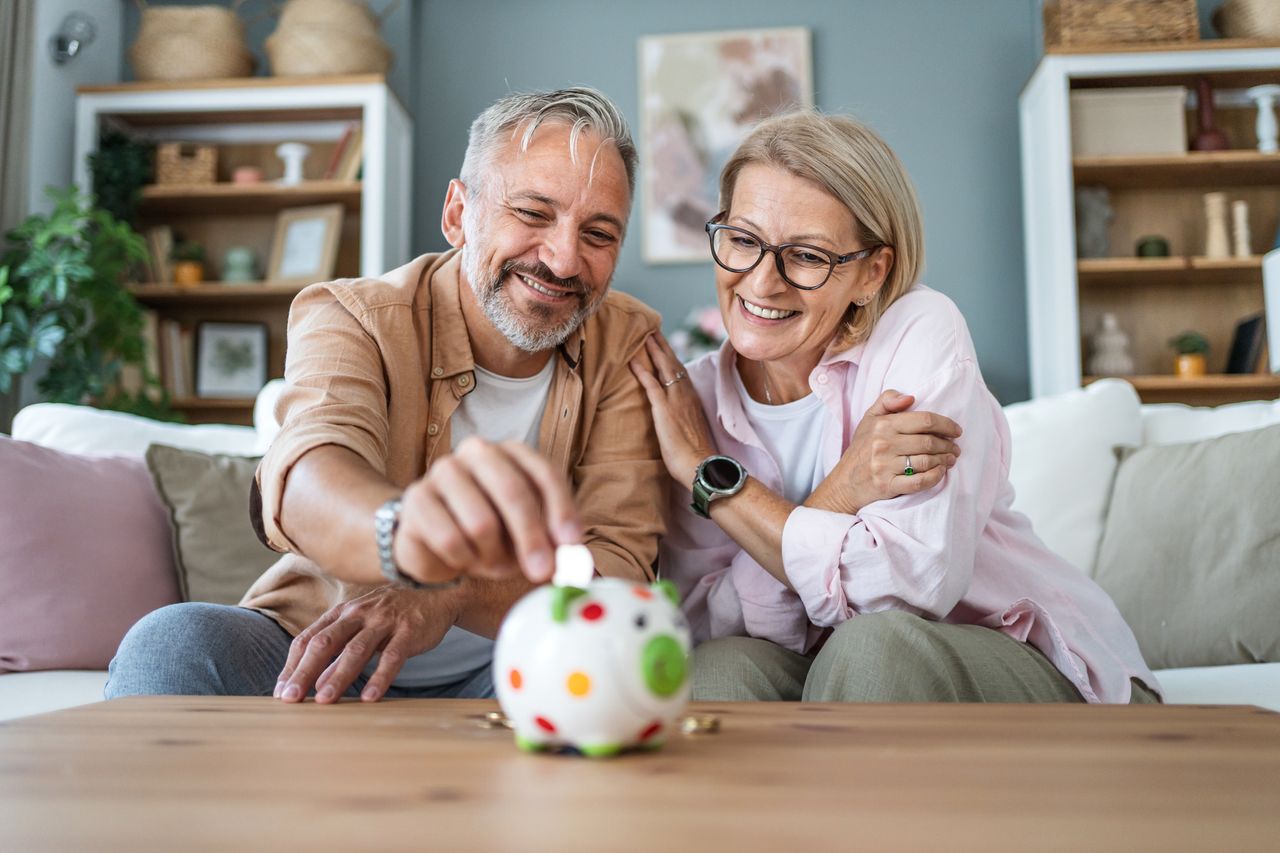 A middle-aged couple putting coins into a piggybank, representing investing into their pensions or Sipps