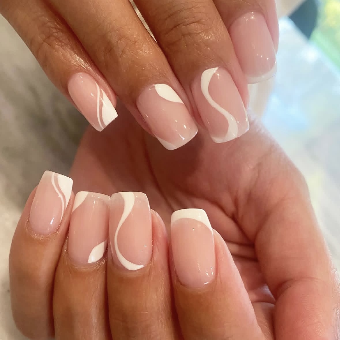 A nude manicure with white swirl designs.