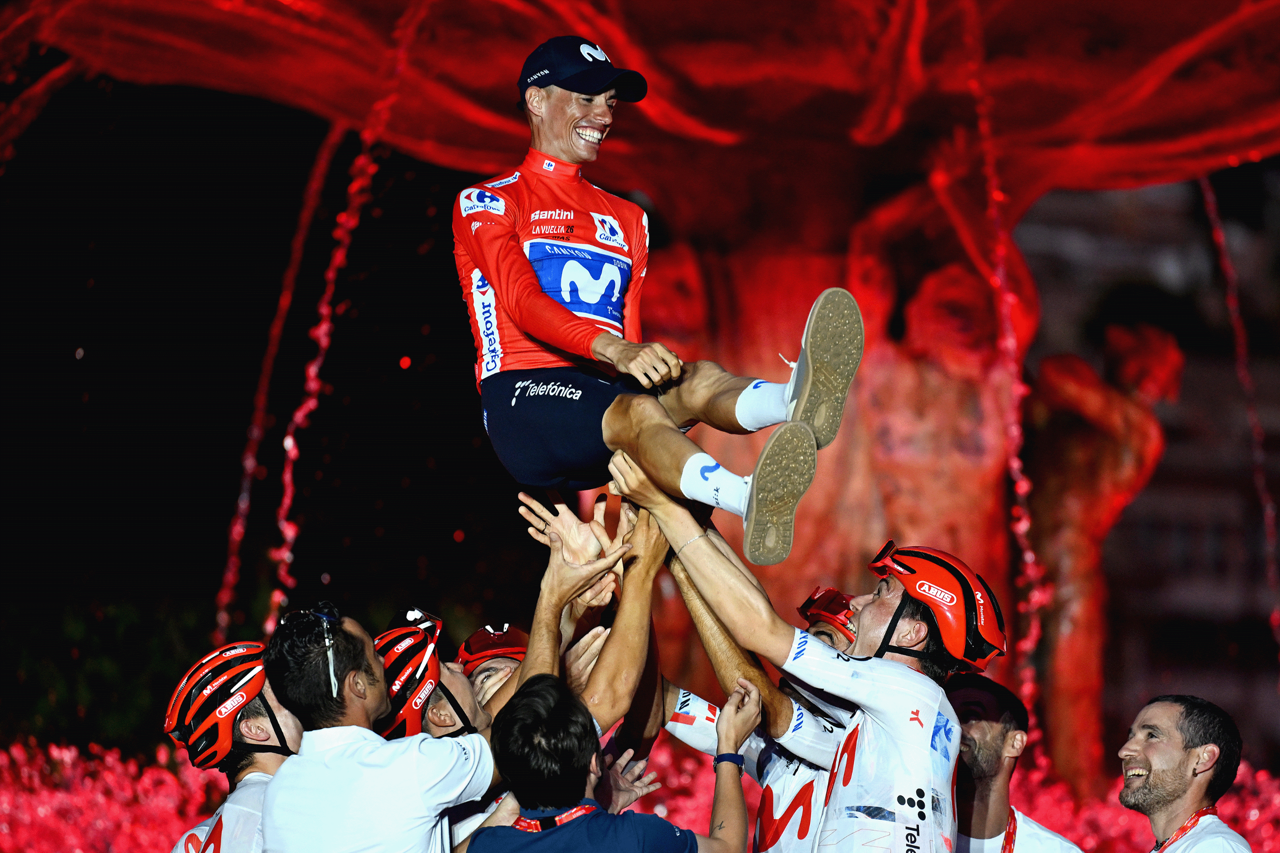 Mas is tossed into the air by his teammates and staff in front of a red-tinged fountain