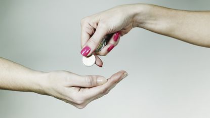 A woman drops coins into the open palm of another woman.