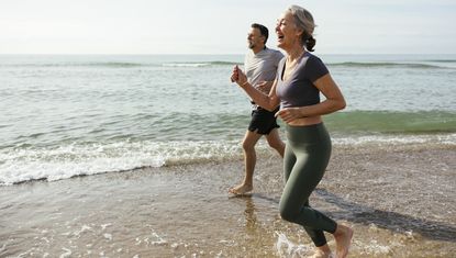 Happy mature couple laughing and running in water at beach