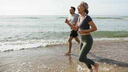 Happy mature couple laughing and running in water at beach