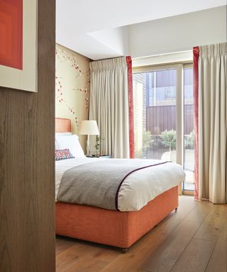 An example of bedroom curtain ideas showing taupe curtains with an orange velvet lining in a bedroom with an orange bed and wooden flooring
