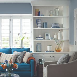 A living room in a white and blue colour scheme with a white bookshelf decorated with books and home accessories