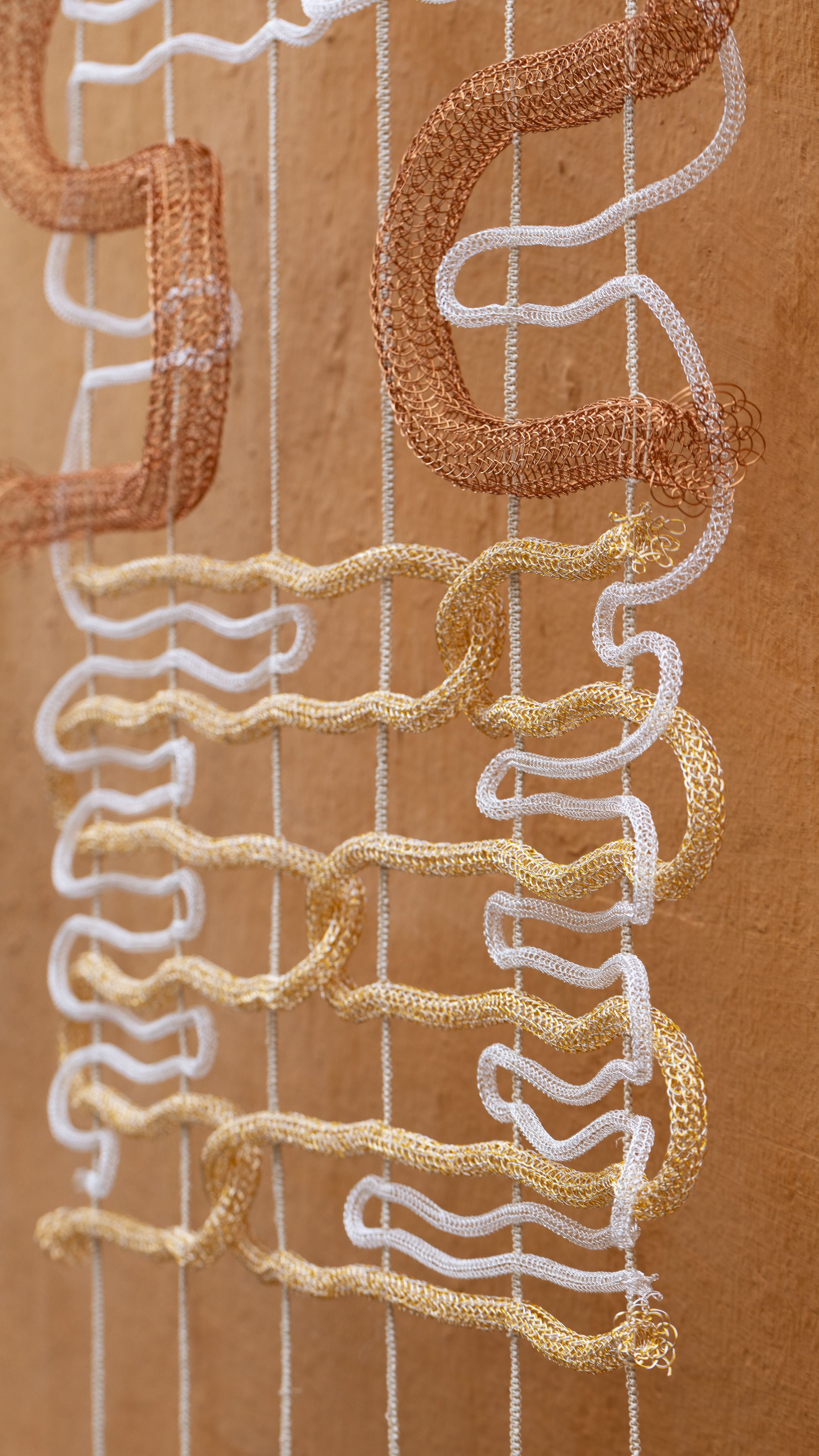 Close-ups of artisanal works in textile and polished stone, and a portrait of two artisans, a man and a woman, sitting in front of a gradient fabric panel in tints of green, blue, orange, and white.