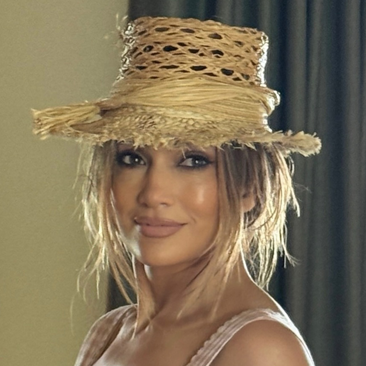 J.lo wears a straw hat, gingham-print dress, and straw tote bag.