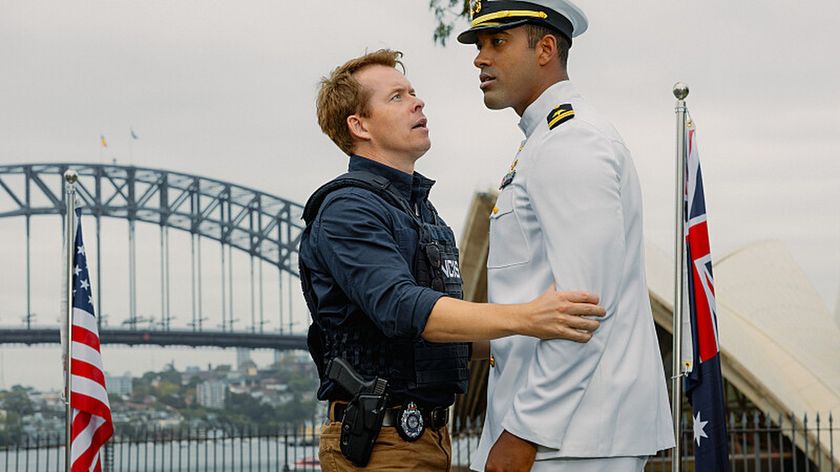 JD (Todd Lasance) grabbing Lt. Oscar Daniels (Damon Manns), with Sydney Harbour Bridge and the Australia and US flags visible in the background, in NCIS Sydney season 3