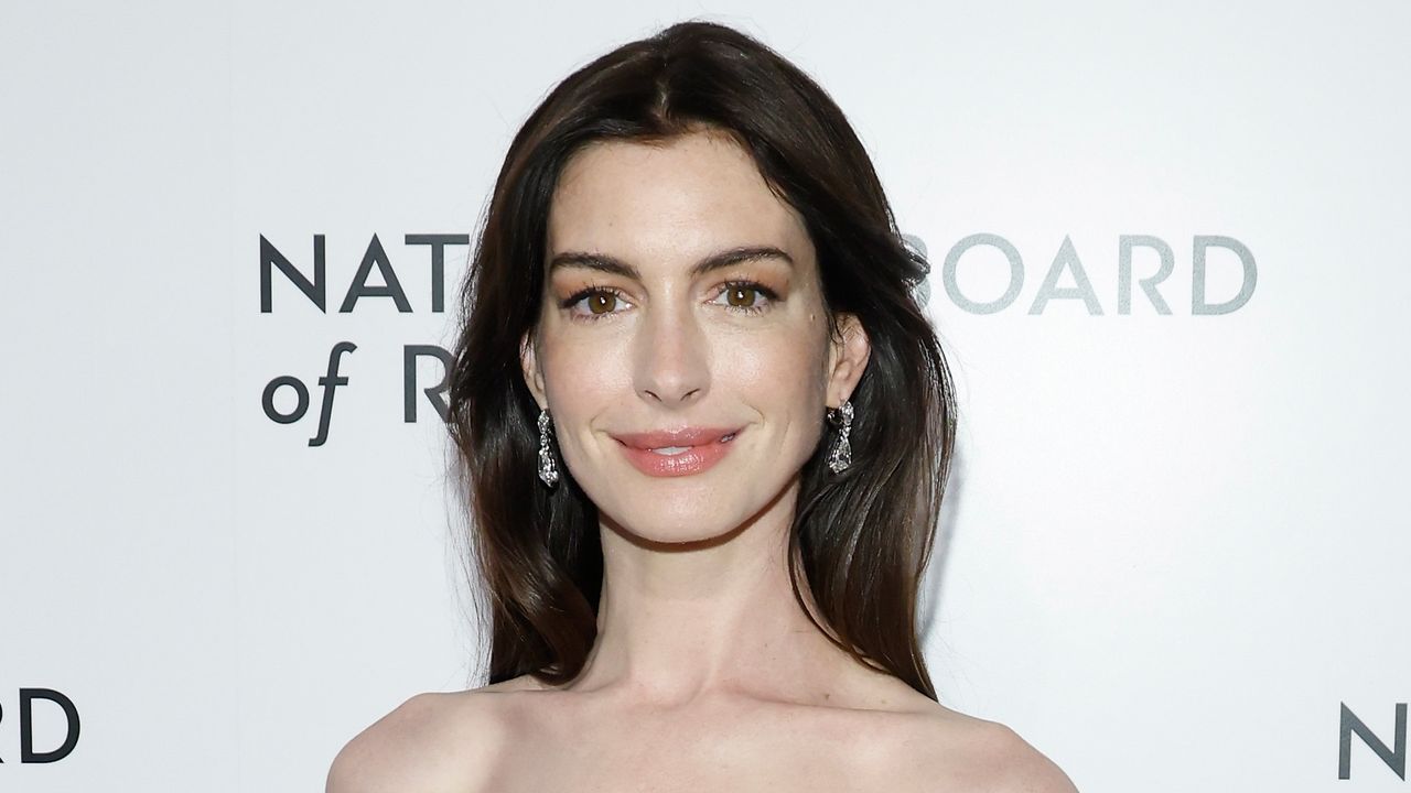 Anne Hathaway is wearing a black sleeveless dress. She is standing and giving a smile to the camera. 