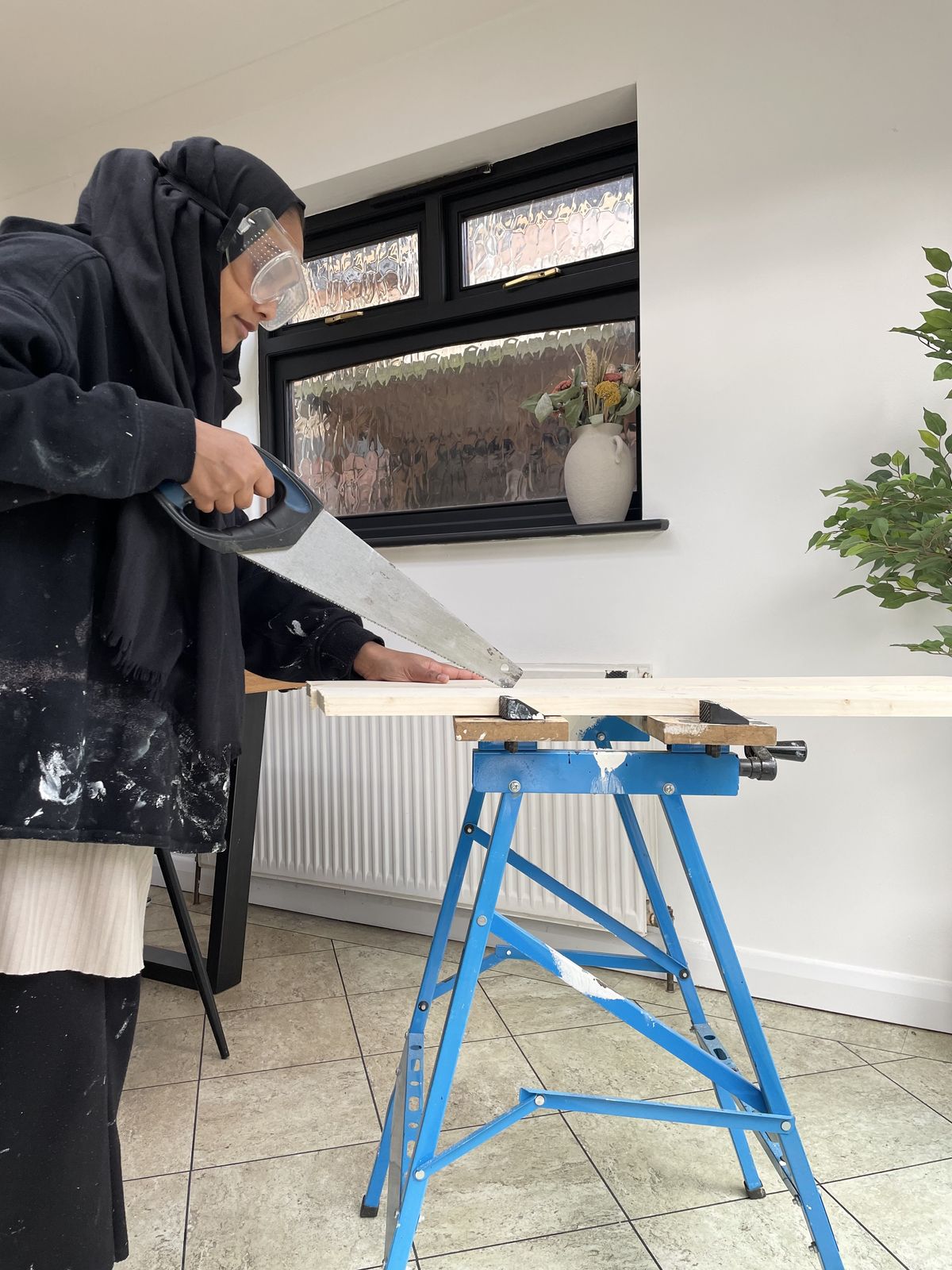 A woman uses a handheld saw to cut a piece of wood to size