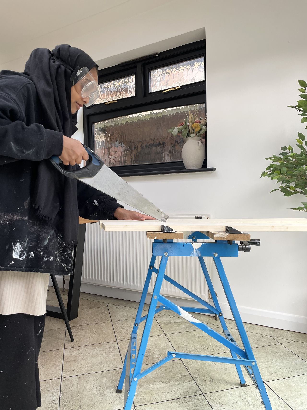 A woman uses a handheld saw to cut a piece of wood to size