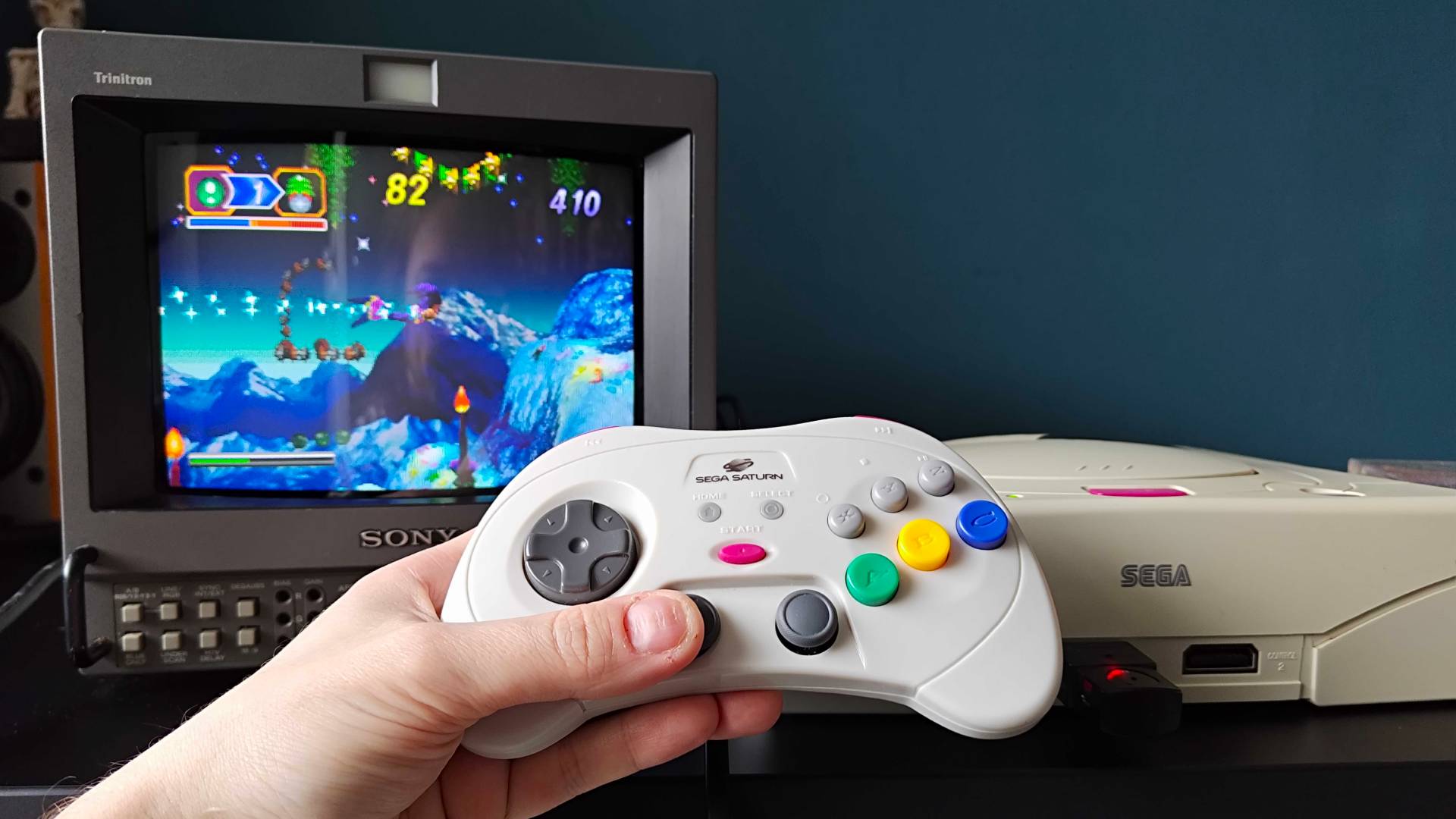 Hand using Retro-Bit Sega Saturn Pro controller to play Christmas Nights into Dreams on white console connected to Sony PVM CRT TV.