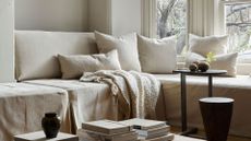A cozy white living room with layered throws, pillows, and stacks of books with vases