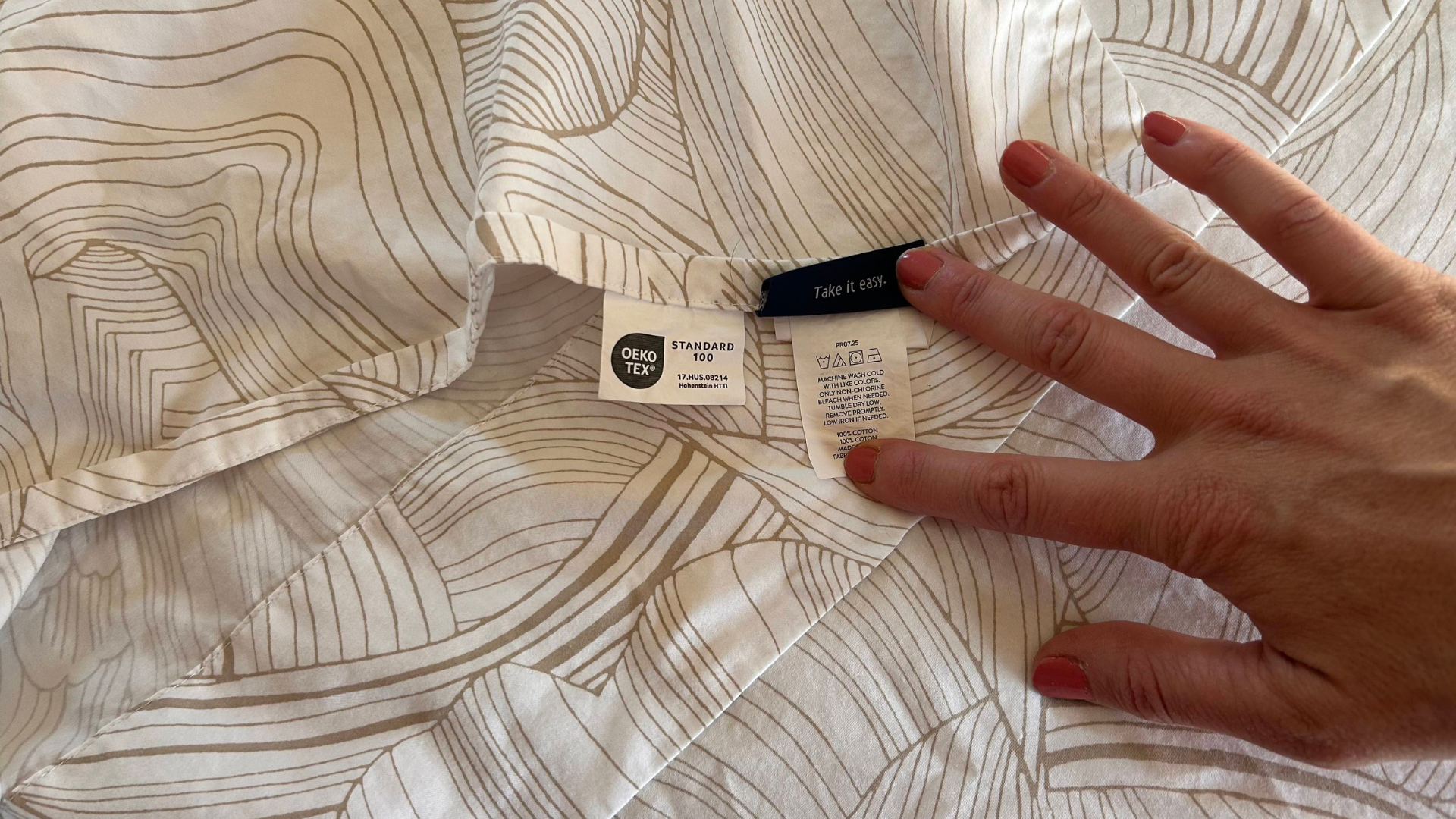 Hand placed on the Brooklinen Luxe Sateen Core Sheet set showing the care tag