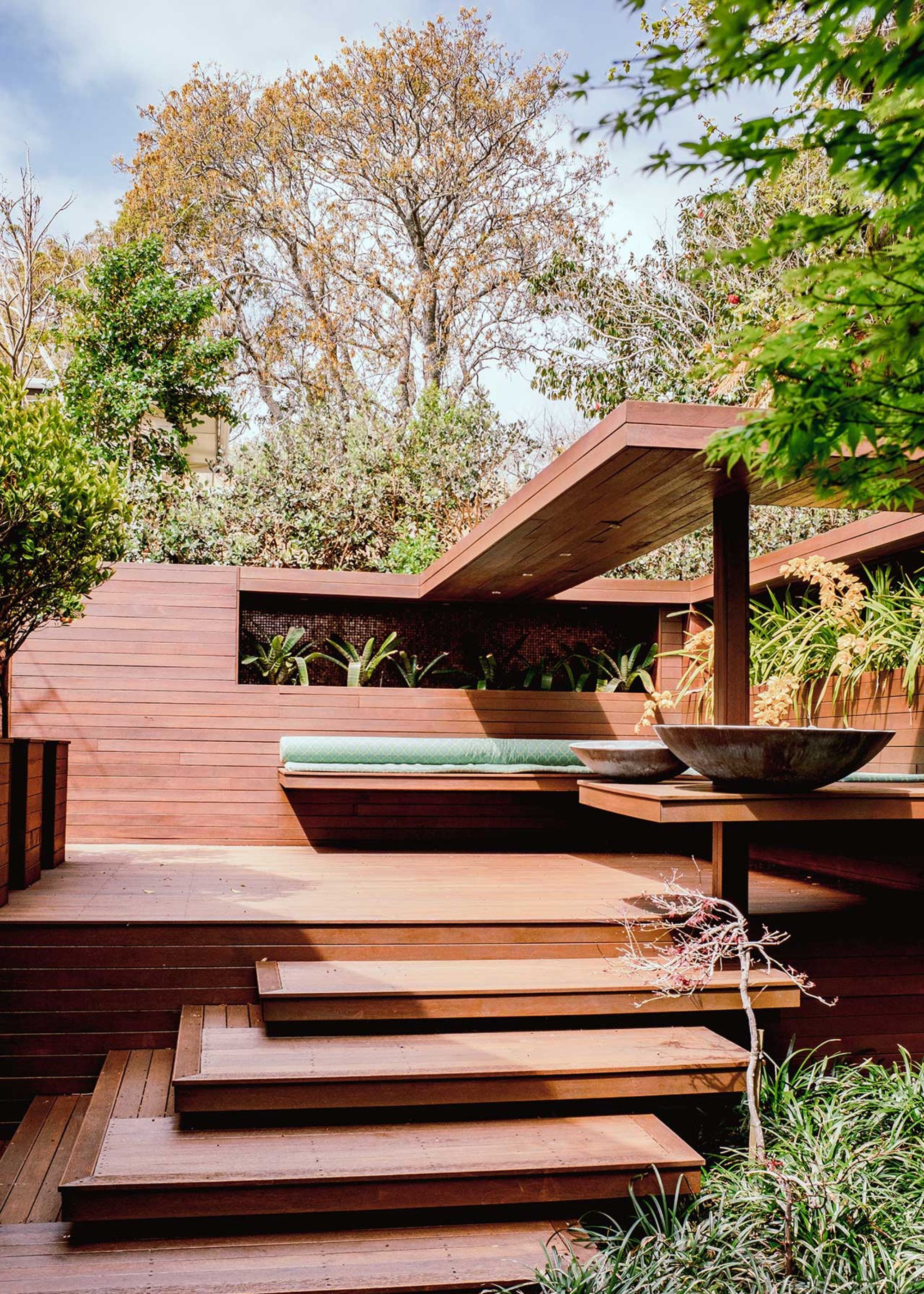 Brown decking with a staircase leading to a decking seating area that has a cozy cushion seating feature.