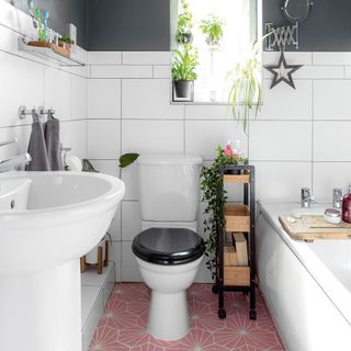 Grey bathroom with white tiles, pink stencilled flooring and houseplants