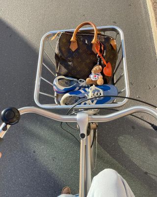 Photo taken from fashion influencer @lunaisabellaa's perspective as she's riding a bicycle with a chic pair of blue Adidas on-trend sneakers and Lous Vuitton bag in the basket.