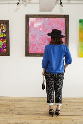 A woman stands in an art gallery admiring a piece of art on the wall