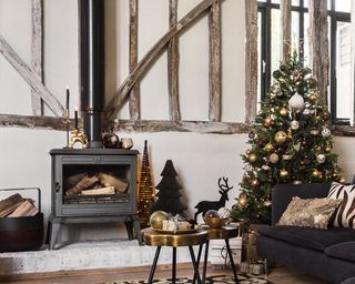 A traditional Christmas living room with wooden beams, wood burning stove and Christmas tree with metallic baubles and star Christmas tree topper