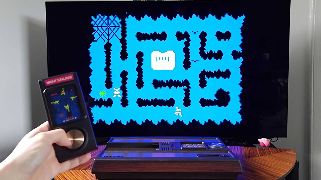 Hand holding Intellivision Sprint controller with Night Stalker gameplay on TV in backdrop.