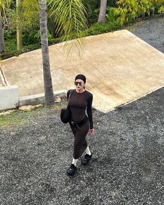 Woman wears a brown body-con dress, low hip belt, Nike x Jacquemus sneakers and white socks.