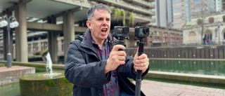 A man holding up two action cameras next to each other and yelling