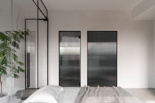 A bedroom with white walls and tinted glass doors for the bathroom