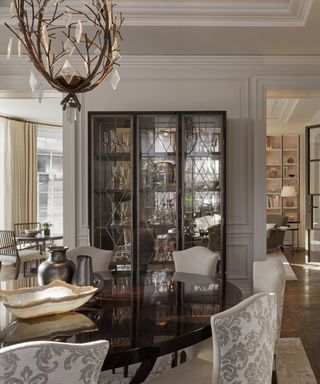 A black and white dining room with a nature-inspired chandelier and a glass and black china cabinet