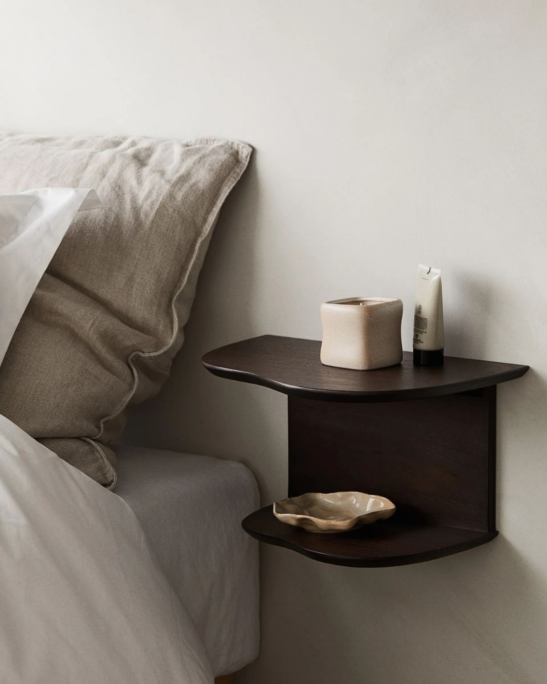 Wall Shelf in dark wood with wavy structure, against beige wall.
