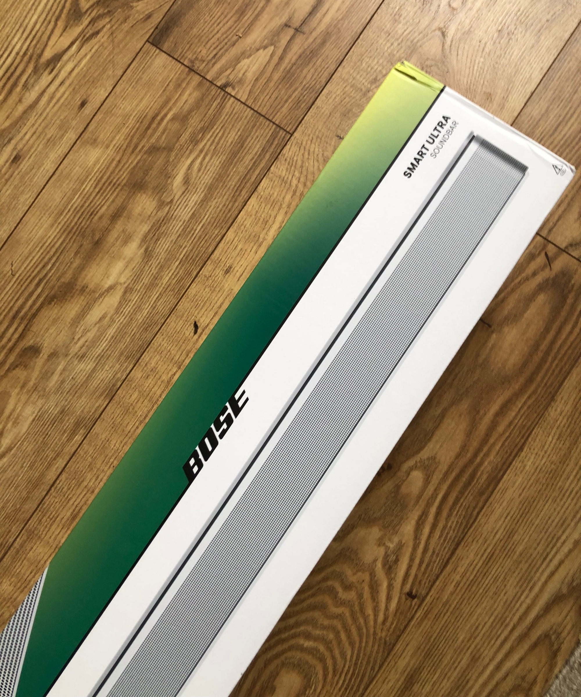 Bose Smart Ultra Soundbar in green and white packaging on wooden floor in Dan Fauzi's home.