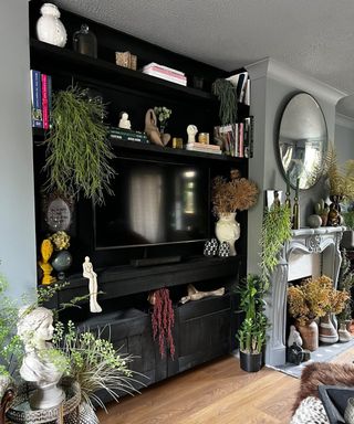 Dark living room wall with cabinet and TV mounted into it, surrounded by plants and objet d'art