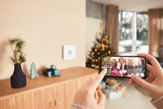 A living room decorated for Christmas with a family viewing their Ring doorbell footage on a phone