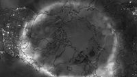 grey scale image over the northern hemisphere, showing a white wispy circle of aurora.