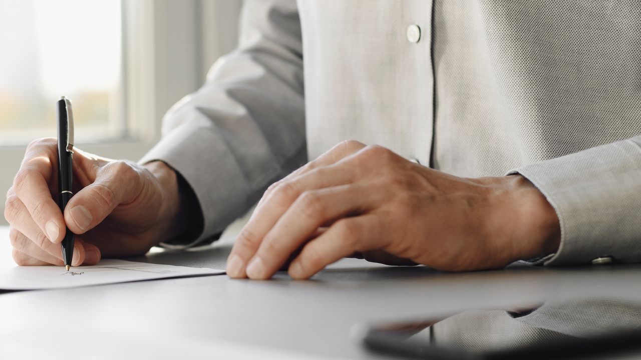 A man, only his hands a shirt showing, writes a letter.