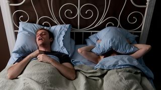 Man snoring while partner presses a pillow over their head in frustration