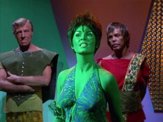 a green-skinned woman in a crop top on a futuristic-looking tv set