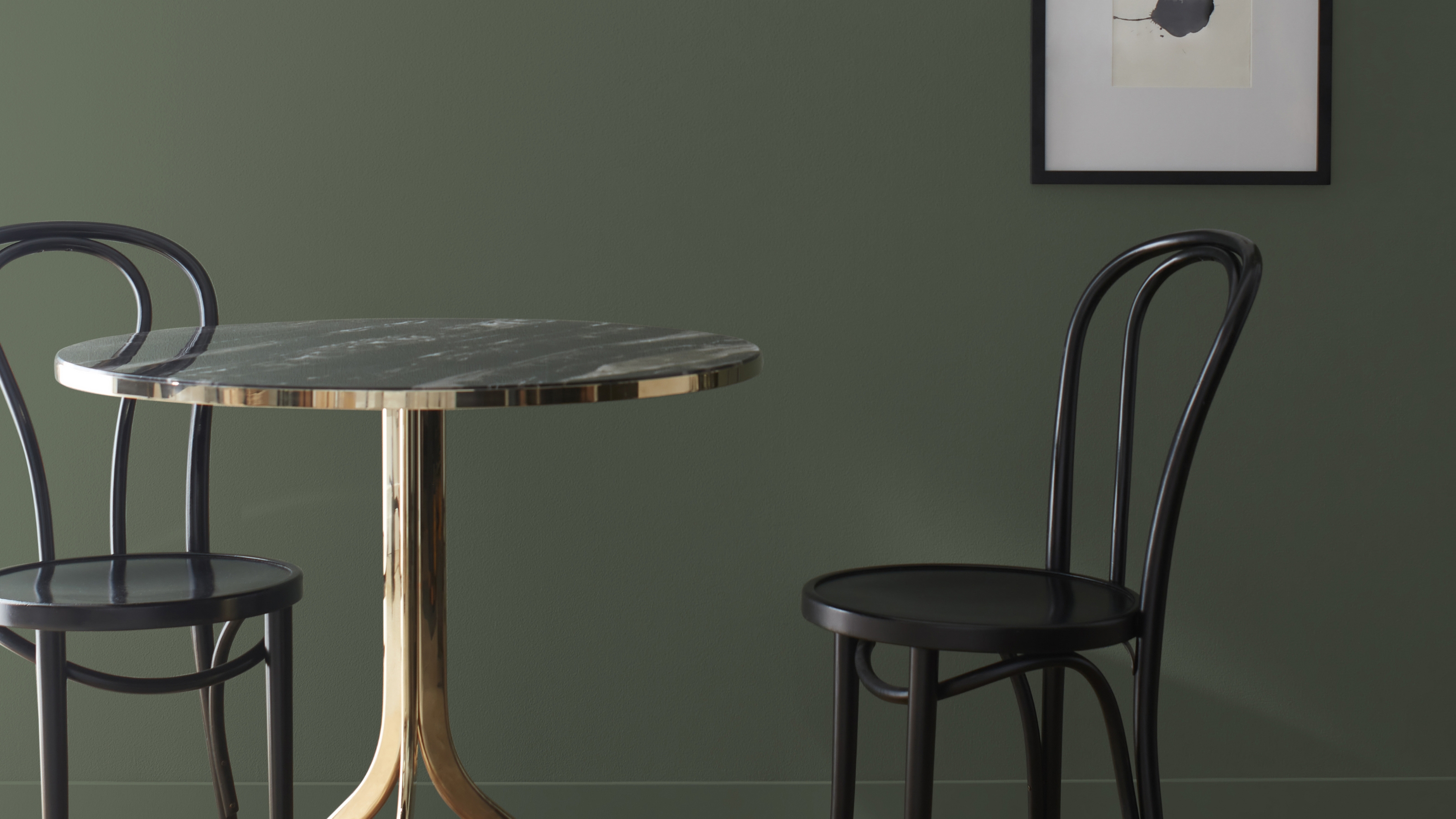 Close-up image of a bistro table and two matching chairs in a room that's painted in a dark forest green.