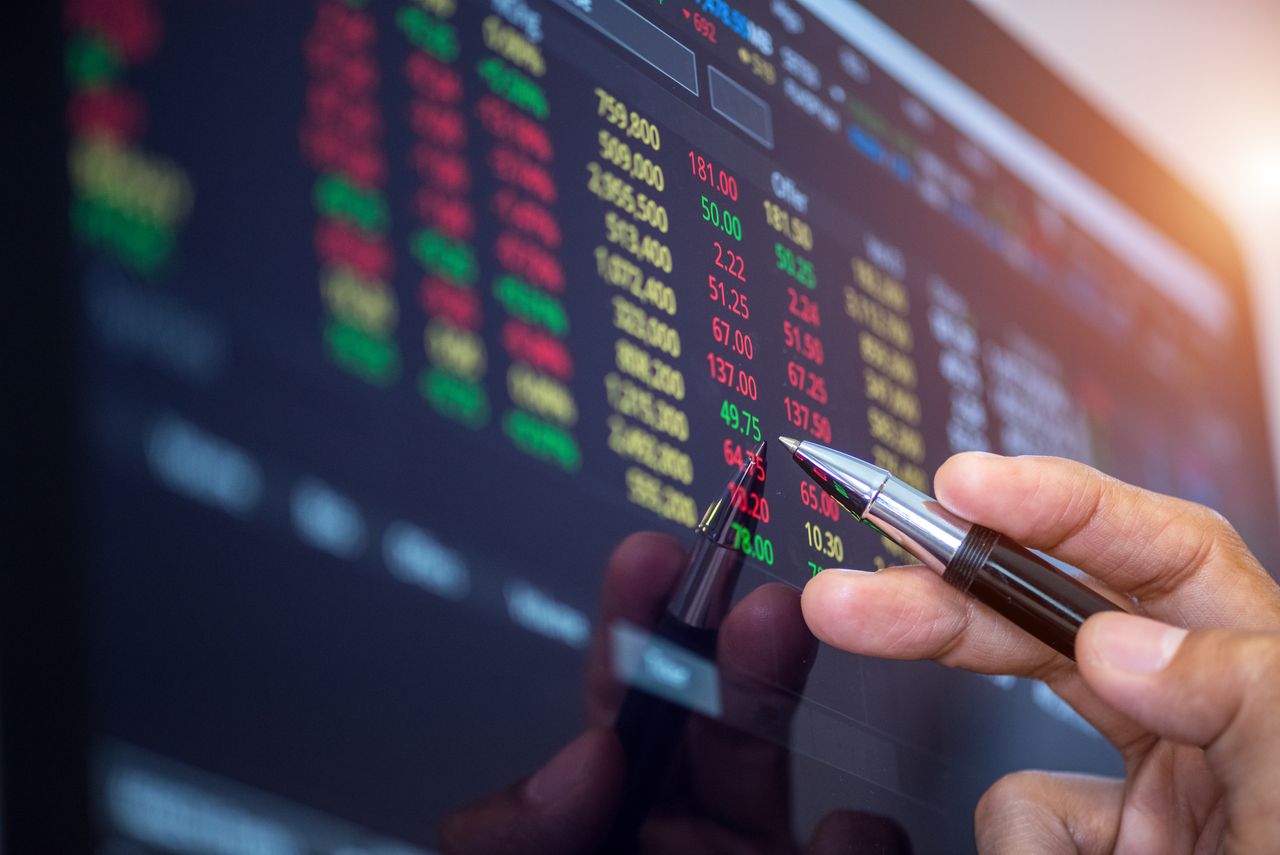 closeup of person looking at stock prices on screen and holding a pen