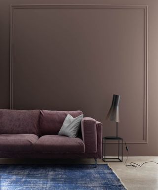 dark brown wall with purple velvet sofa, blue rug and table with lamp