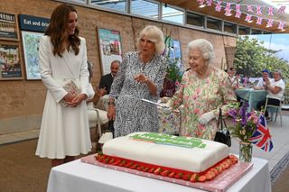 The Queen (C) considers cutting a cake with a sword, lent to her by The Lord-Lieutenant of Cornwall, Edward Bolitho, to celebrate of The Big Lunch initiative at The Eden Project during the G7 Summit on June 11, 2021 in St Austell, Cornwall, England.