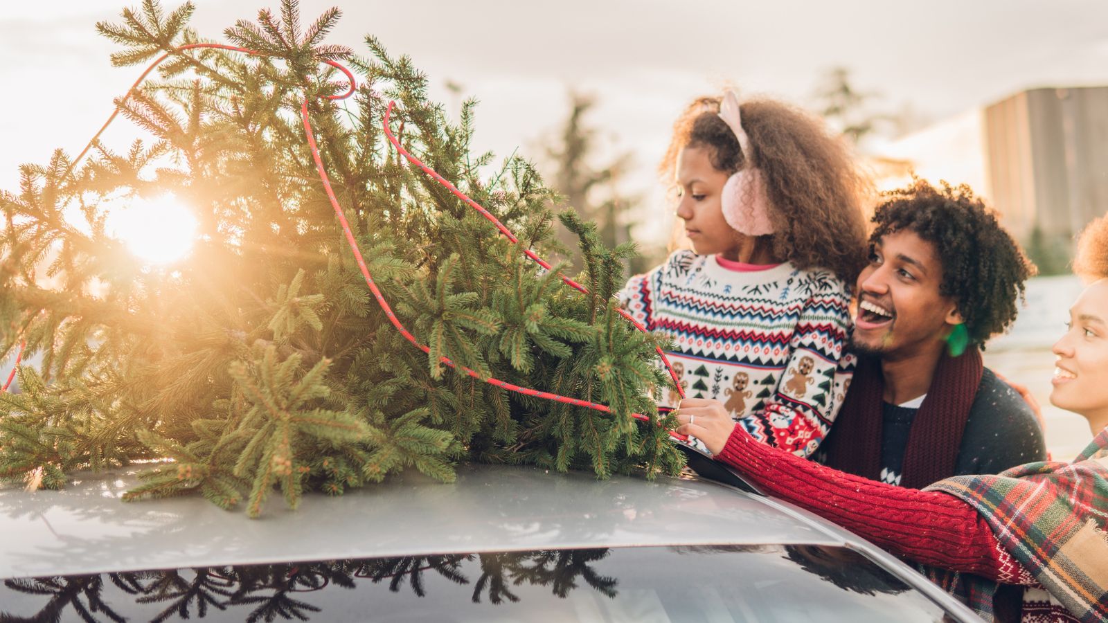 Christmas tree tied to a car roof by happy couple and their daughter