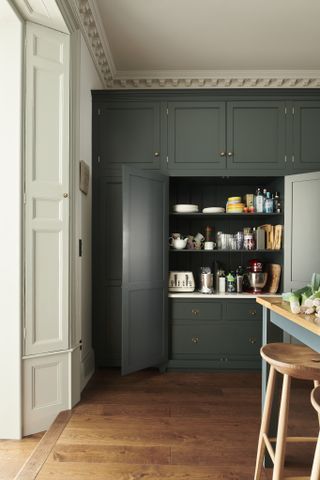 A dark green kitchen cabinet with bi-fold doors disguising an appliance countertop and shelving