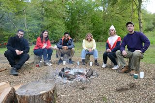 The Outsiders contestants sitting around a campfire: Jamali Maddix, Jessica Knappett, Toussaint Douglass, Kerry Godliman, Lou Sanders and Ed Gamble